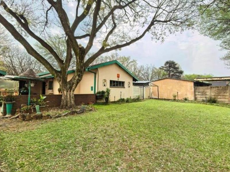 Spacious rear garden featuring a large lawn, mature trees, a detached garage, and a brick boundary wall, offering potential for outdoor landscaping.