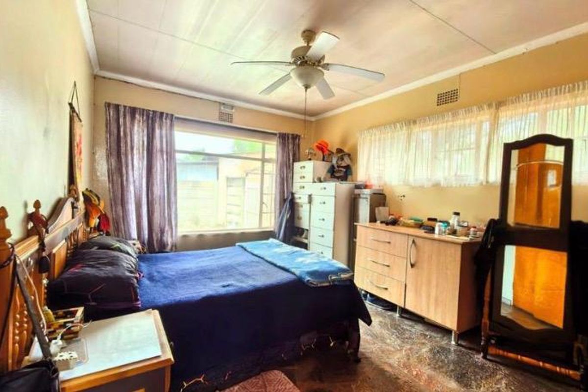 A bedroom featuring a ceiling fan, large windows for natural light, and tiled flooring. The space requires cosmetic updates to improve its overall condition.