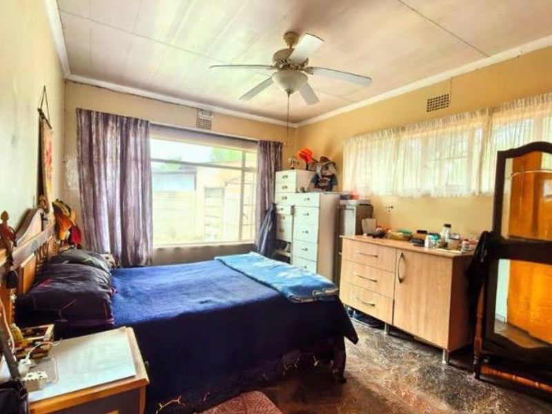 A bedroom featuring a ceiling fan, large windows for natural light, and tiled flooring. The space requires cosmetic updates to improve its overall condition.