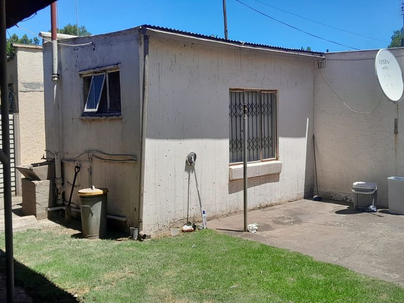 Rear exterior view of the property featuring a concrete patio, security bars on windows, and a corrugated metal roof structure.