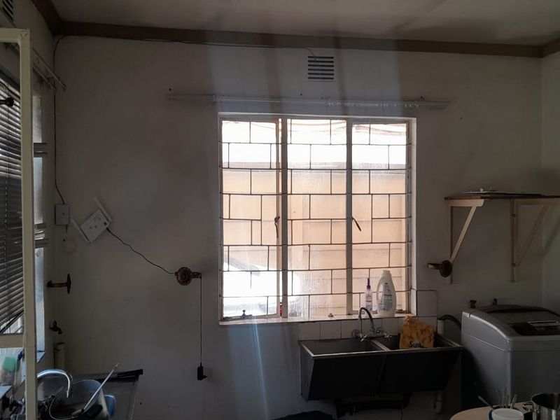A functional laundry area featuring a double stainless steel sink, security burglar bars on the window, and wall-mounted shelving for storage.