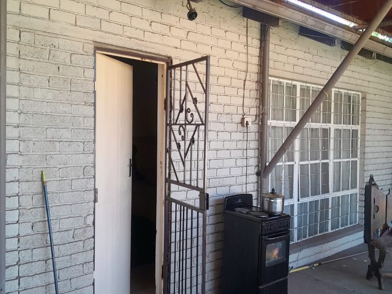 A covered outdoor patio area featuring painted brick walls, security gate, and window bars, offering a functional space for outdoor living.