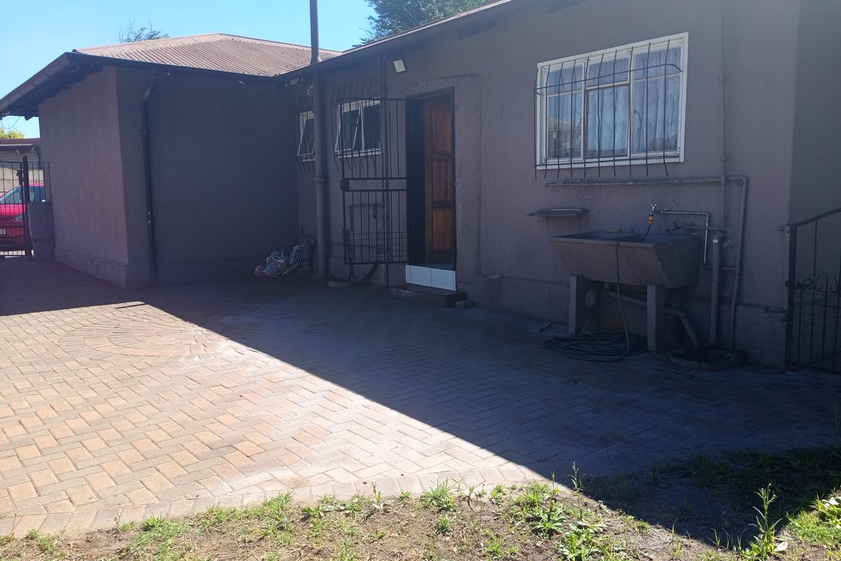 Rear exterior view of the property featuring a paved courtyard area, utility sink, and security bars on windows and doors.