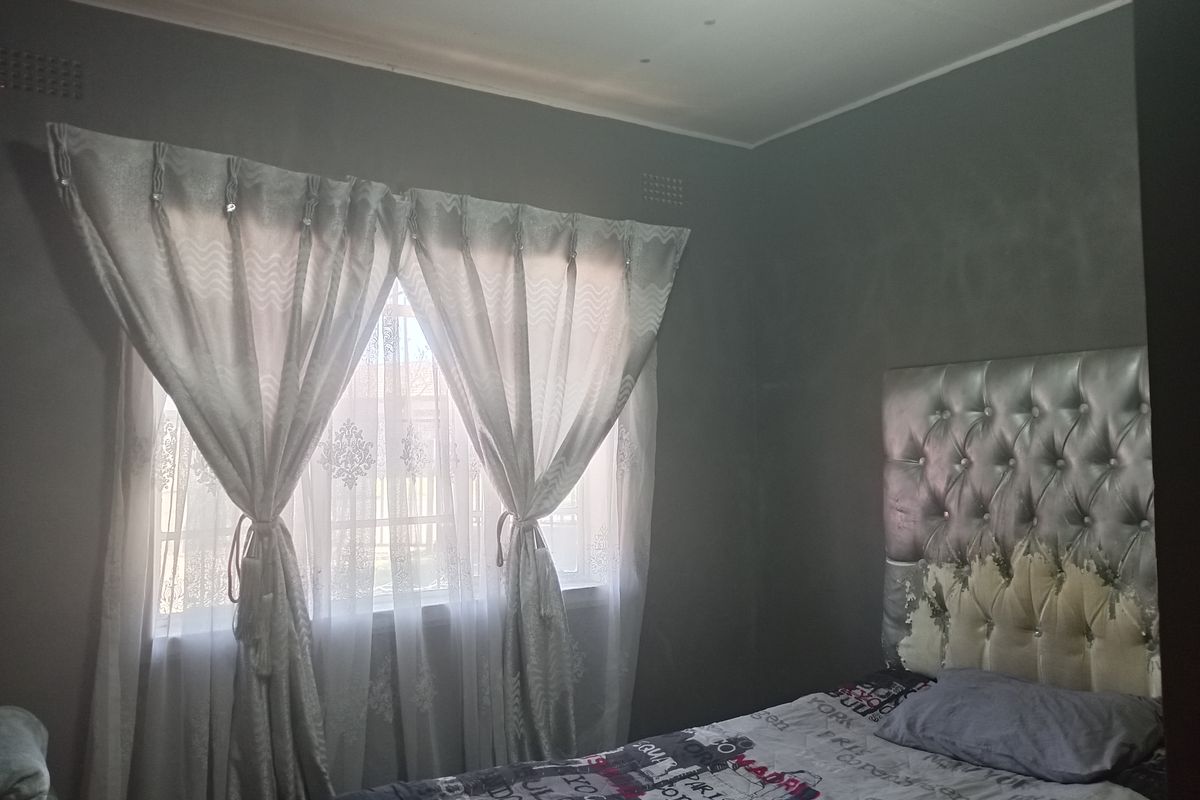 A bedroom featuring grey painted walls, a window with security bars, and decorative ceiling cornicing.