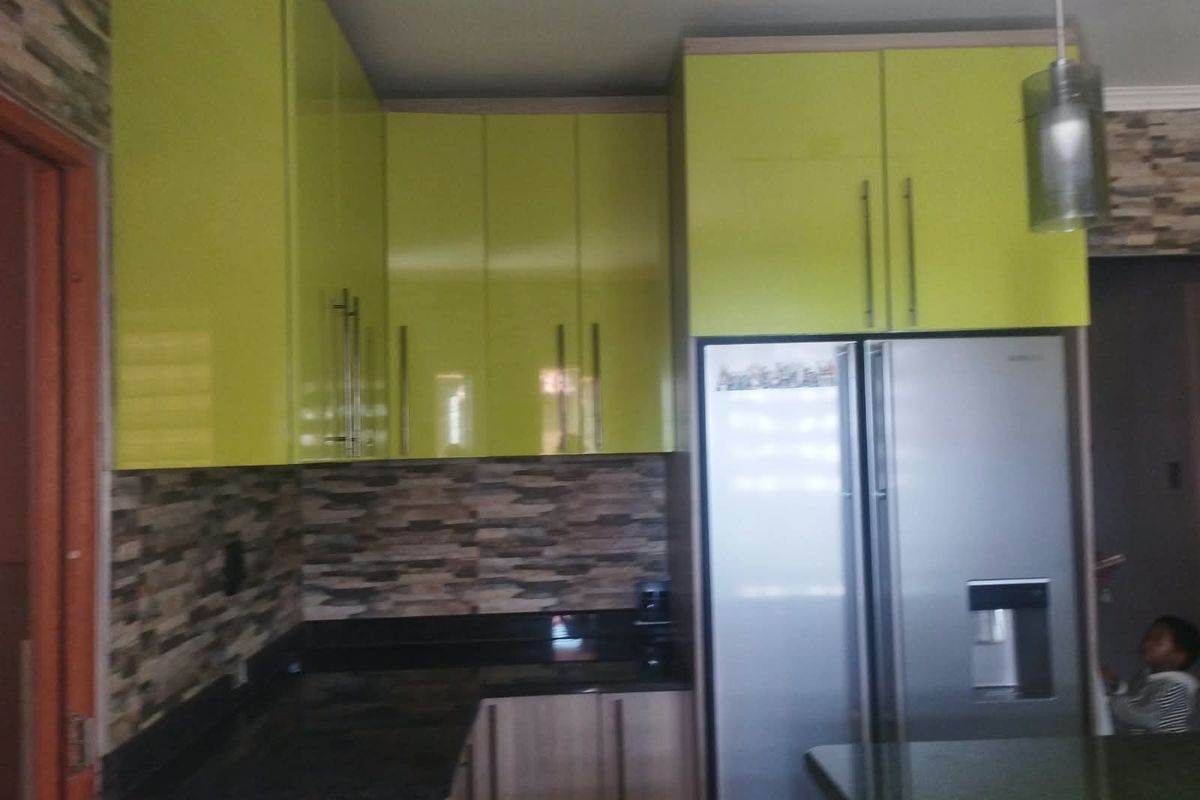 A kitchen featuring lime green high-gloss cabinetry, dark stone countertops, and a textured stone tile backsplash.