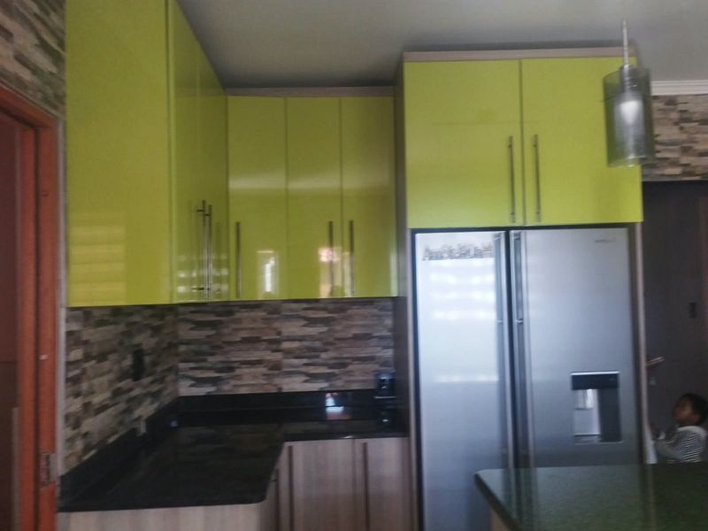 A kitchen featuring lime green high-gloss cabinetry, dark stone countertops, and a textured stone tile backsplash.