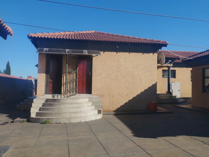 Rear exterior view of the property featuring a paved courtyard, curved concrete entrance steps, and a tiled roof.