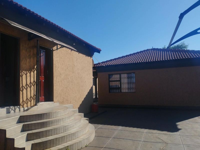 Rear exterior view featuring a paved patio area, curved tiled steps leading to the entrance, and textured wall finishes under a tiled roof.