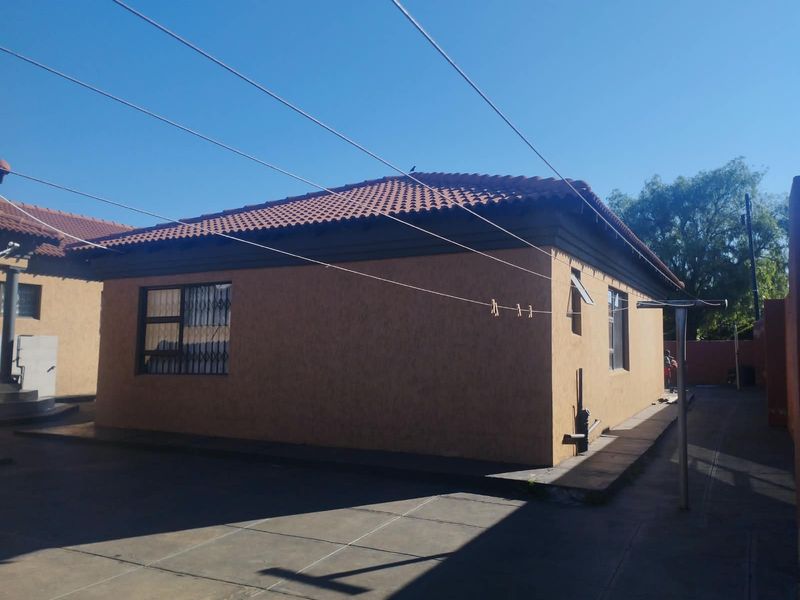 Rear view of the house featuring a tiled roof, concrete paved yard, and security bars on the windows.