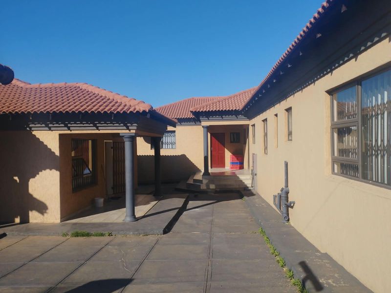A view of the rear courtyard featuring a paved area, covered patio section with columns, and access to the main building entrance.