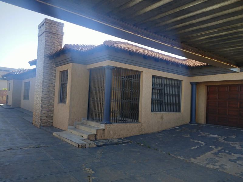Front exterior view of the house featuring a stone-clad chimney, secure entrance with metal gates, a carport, and a garage.