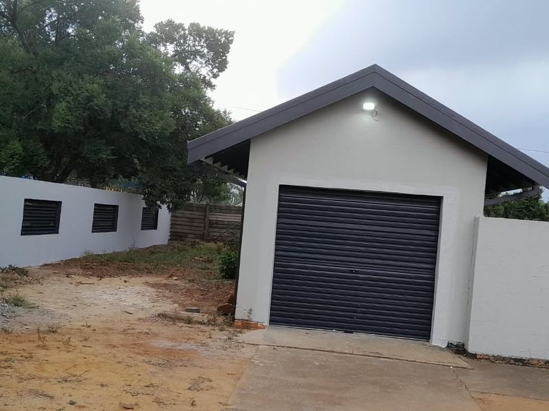 A detached garage with a roller shutter door, featuring a concrete driveway and surrounding perimeter walling in a developing garden space.