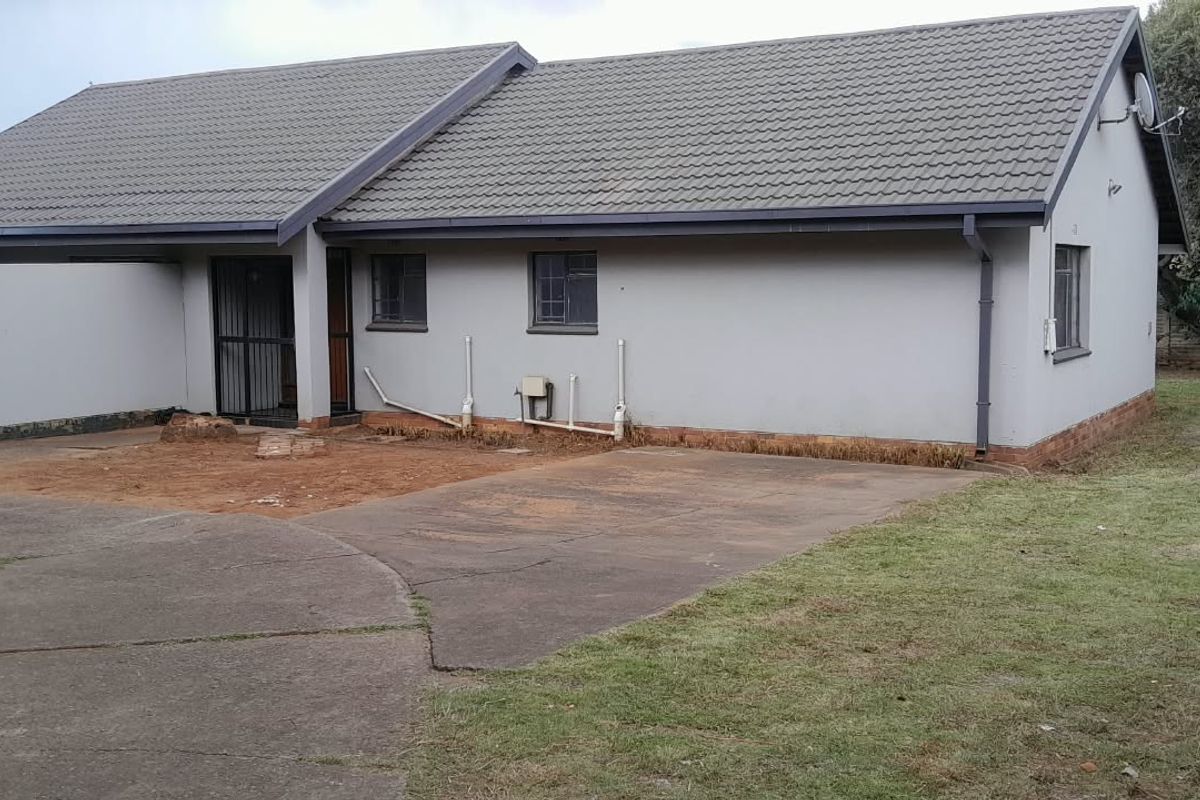 Rear view of the property featuring a concrete driveway, tiled roof, and surrounding garden area with visible exterior maintenance requirements.