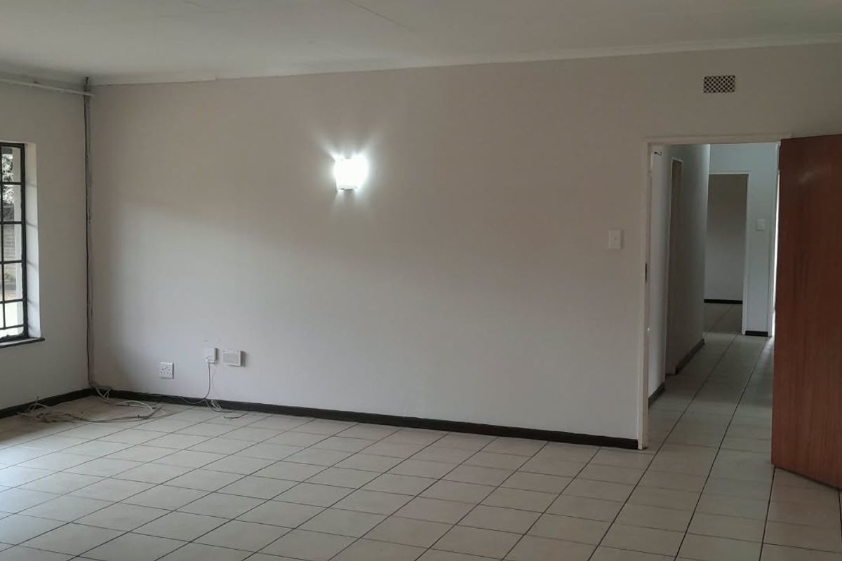 A spacious, empty living room featuring tiled flooring, large steel-framed windows, and wall-mounted lighting, offering a blank canvas for interior design.