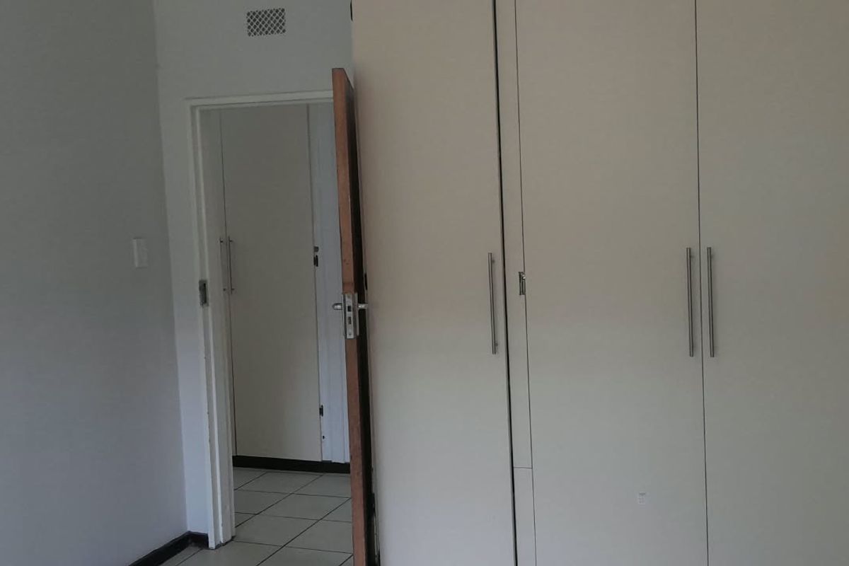 A bedroom interior featuring built-in cupboards and tiled flooring, with a view through the doorway into an adjacent hallway.