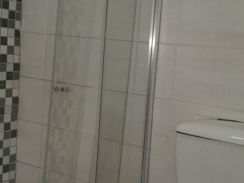 A functional bathroom featuring a glass shower enclosure with a rain shower head, a standard toilet, and contrasting mosaic floor tiling.