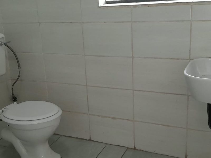 A compact bathroom featuring white wall tiles, a standard toilet, and a wall-mounted basin with a modern black mixer tap.
