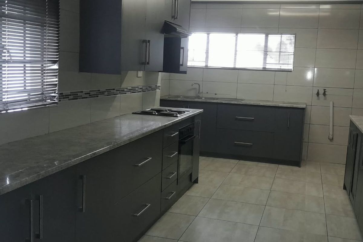 Modern kitchen featuring dark cabinetry, stone countertops, built-in oven and hob, extractor fan, and tiled finishes throughout.