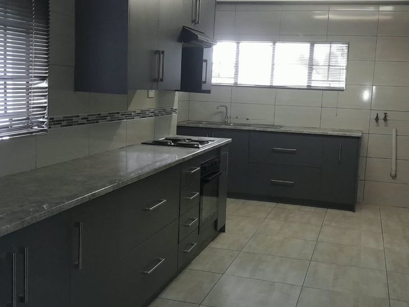 Modern kitchen featuring dark cabinetry, stone countertops, built-in oven and hob, extractor fan, and tiled finishes throughout.