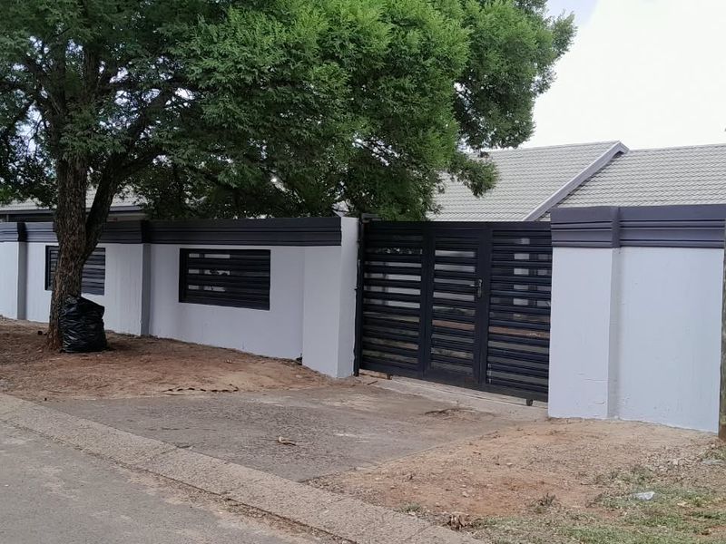 A well-maintained front boundary featuring a modern grey perimeter wall, secure metal driveway gate, and tiled roof visible in the background.