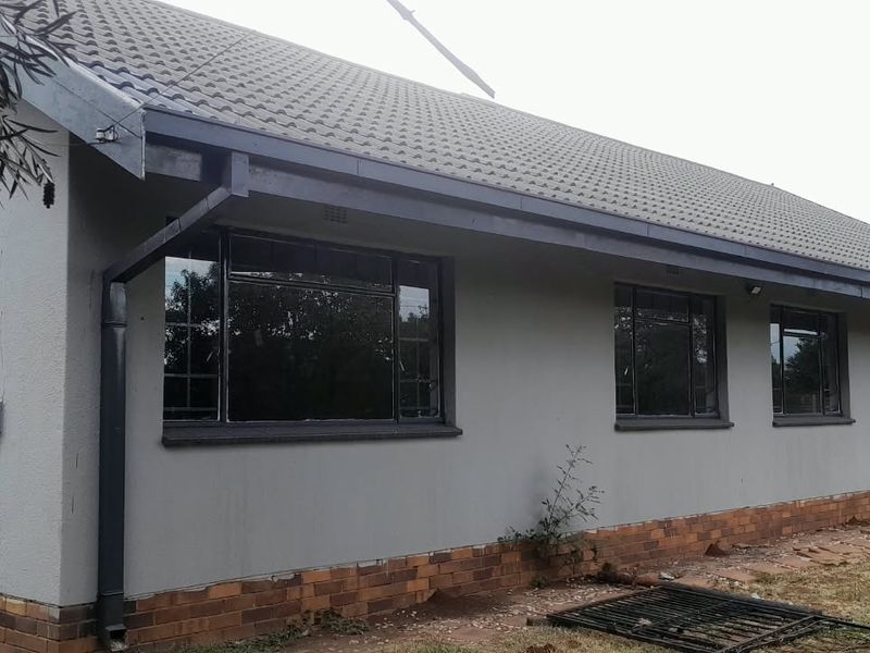 Rear elevation of a single-story house featuring a tiled roof, grey painted exterior walls, and aluminium window frames with security bars.