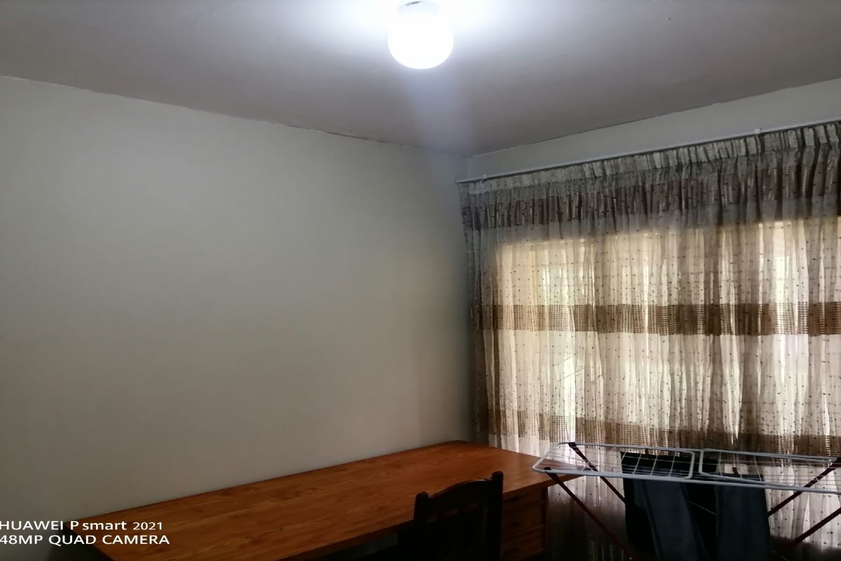 A simple bedroom featuring neutral walls, a large window with curtains, and a central ceiling light fixture.