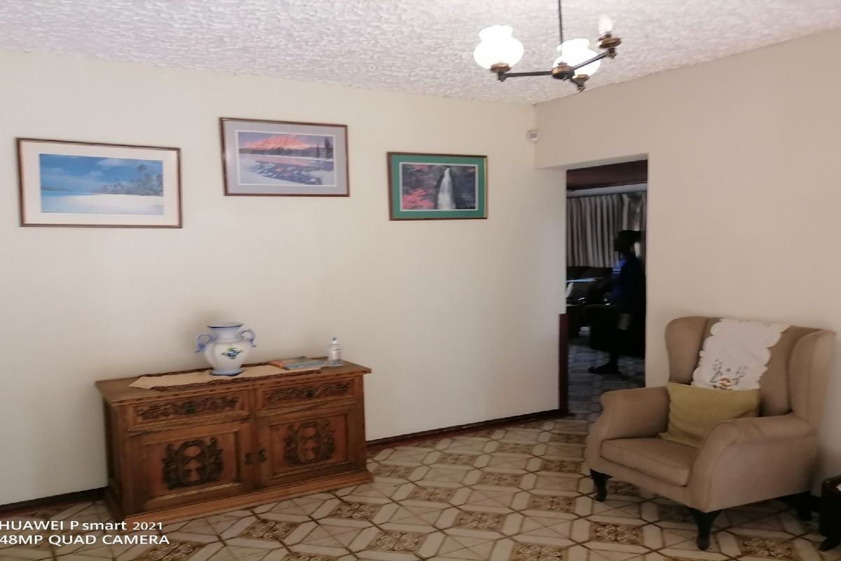 A living area featuring dated floor tiles and a textured ceiling, providing a neutral space with access to an adjoining room.