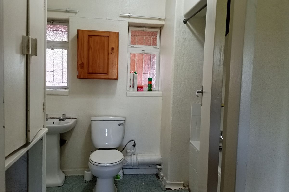 A dated bathroom featuring a pedestal sink, standard toilet, and a shower-over-bath configuration with original fixtures and cabinetry.
