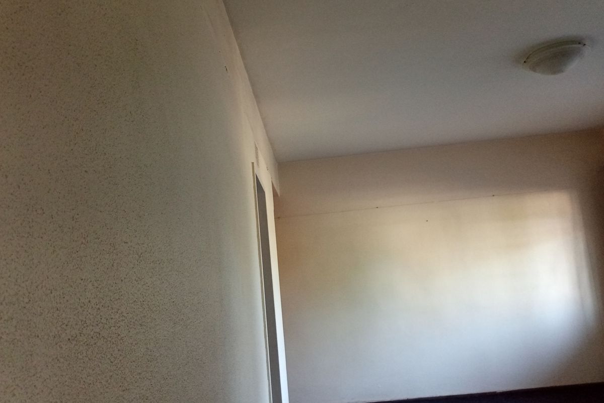 An empty, dated living room featuring textured walls and a simple ceiling light fixture, awaiting renovation and modernization.