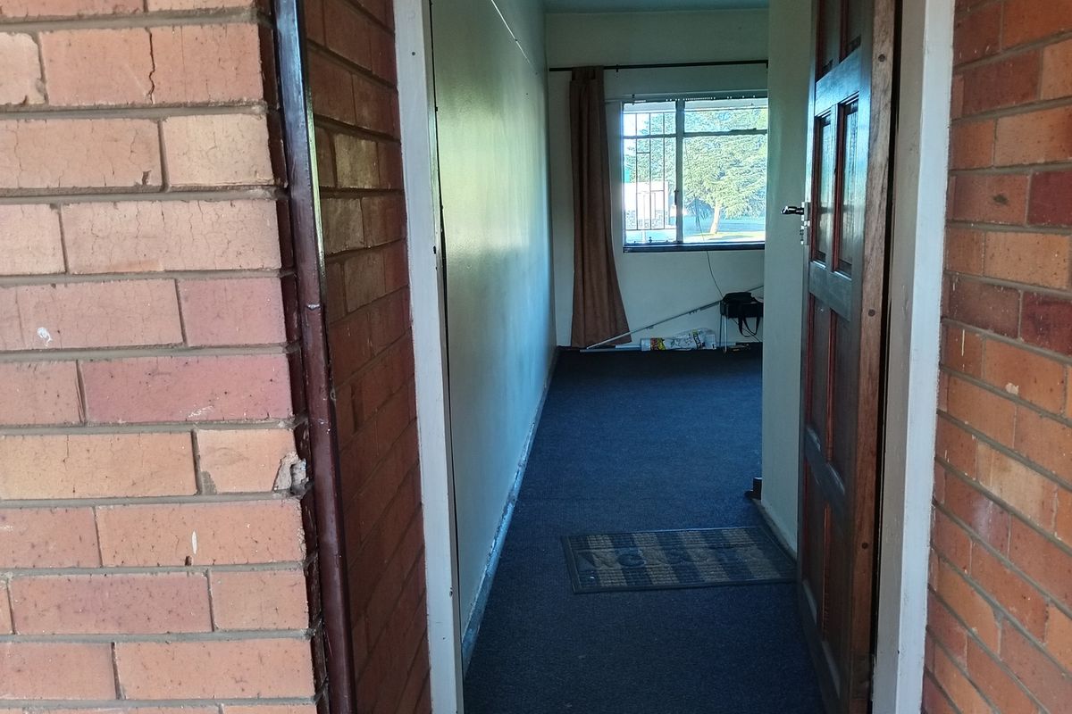 A view through a wooden doorway into a carpeted room with a window, featuring exposed brick exterior walling.