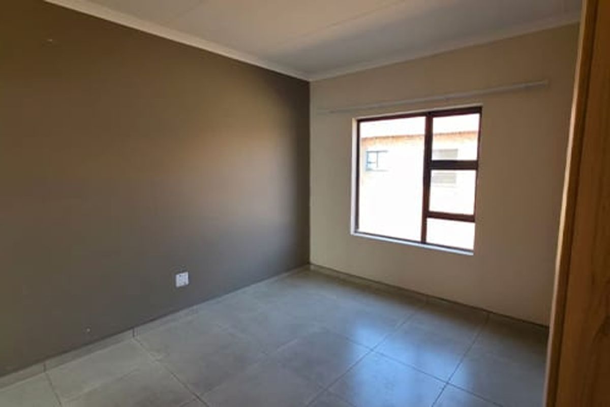 A clean, empty bedroom featuring neutral tiled flooring, a large window with a curtain rail, and a painted accent wall.