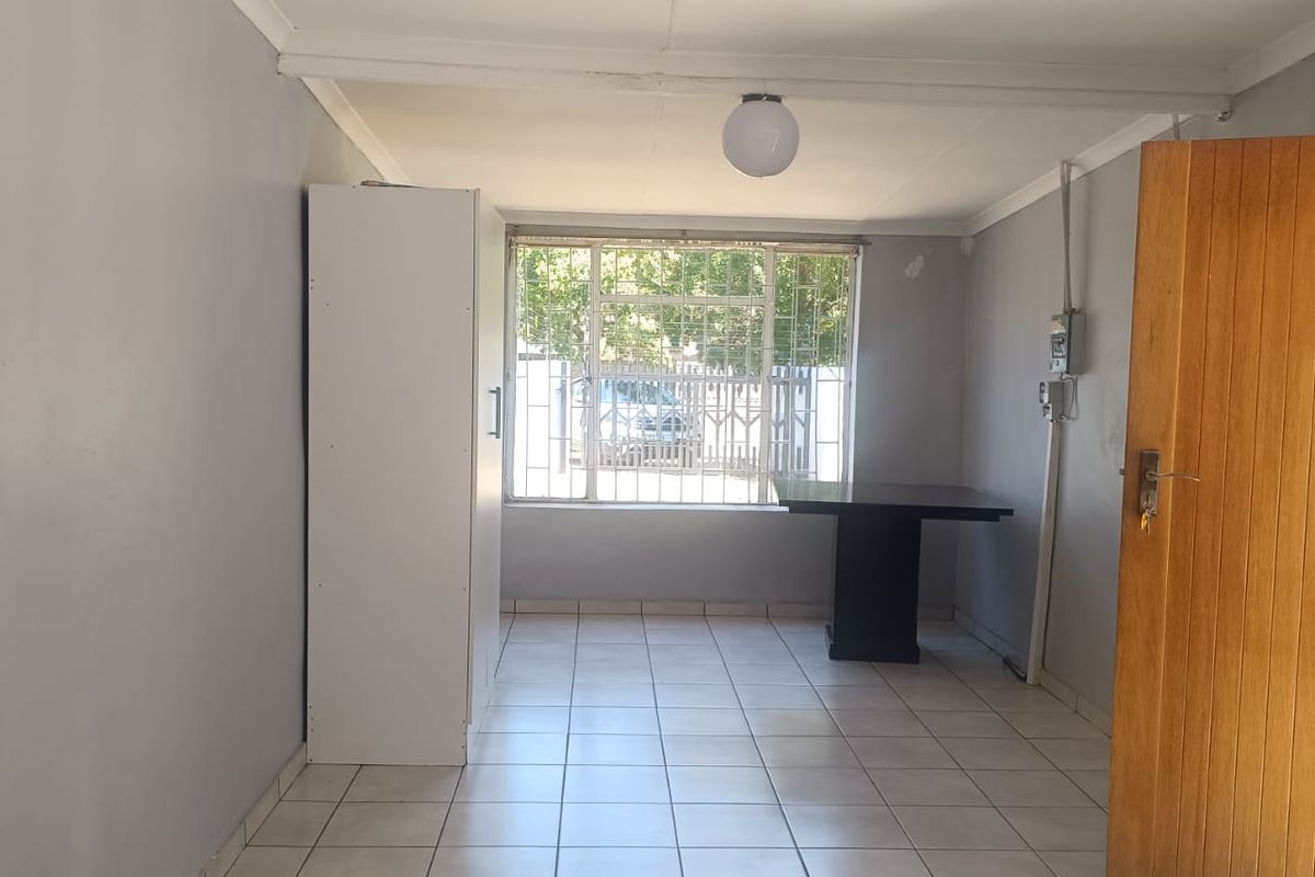 A functional living area featuring tiled flooring, a large window with security bars, and a wooden entrance door.