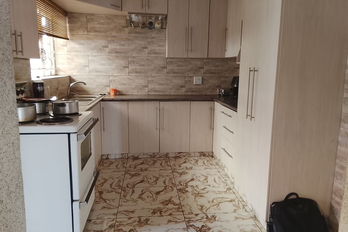 A functional kitchen featuring light wood-finish cabinetry, stone-look tiled backsplash, and patterned floor tiles, equipped with a freestanding stove and double sink.