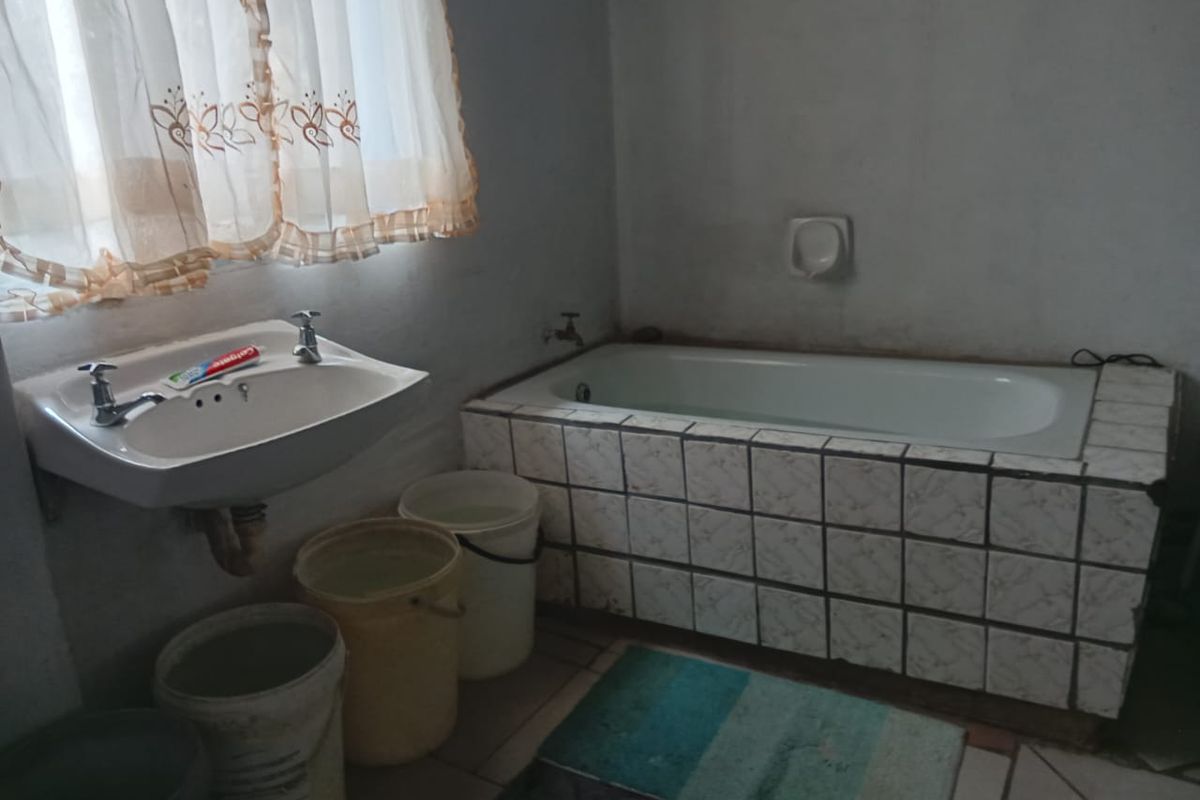 A functional bathroom featuring a standard bathtub with tiled surround and a wall-mounted basin.
