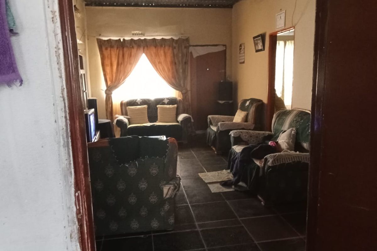 A living room featuring dark floor tiles and an exposed corrugated metal ceiling, providing a basic and functional living space.
