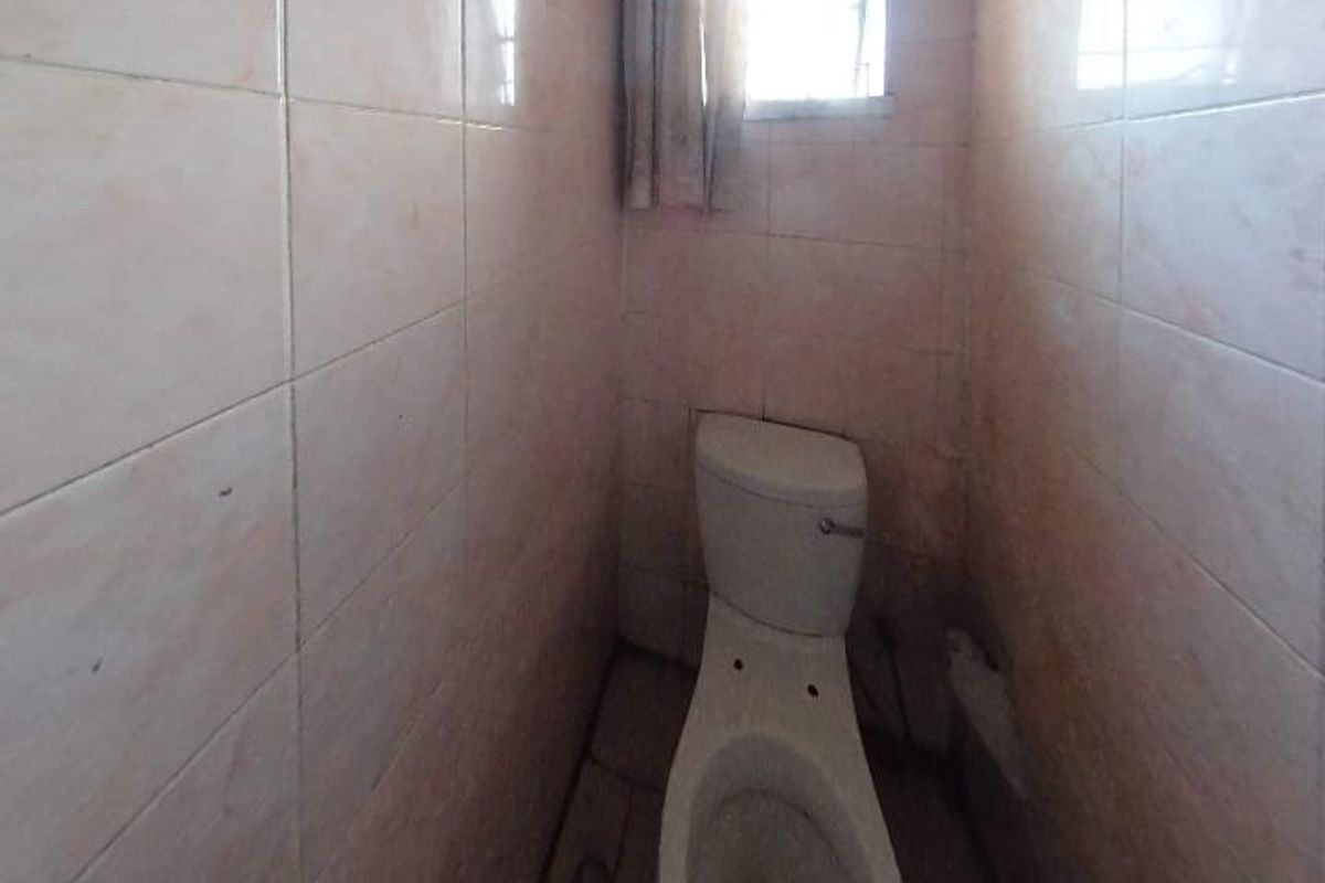 A small, dated bathroom featuring full-height wall tiling and a standard toilet fixture.
