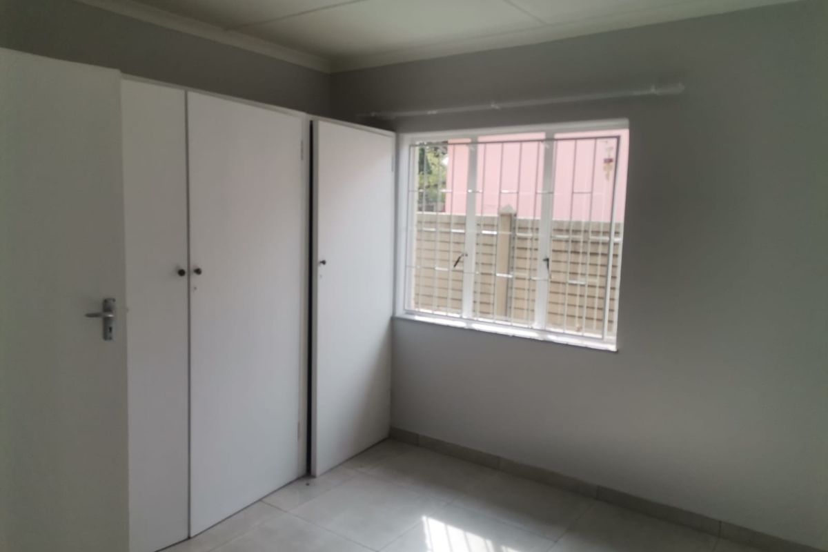 A clean, empty bedroom featuring built-in cupboards, tiled flooring, and a window fitted with security bars.