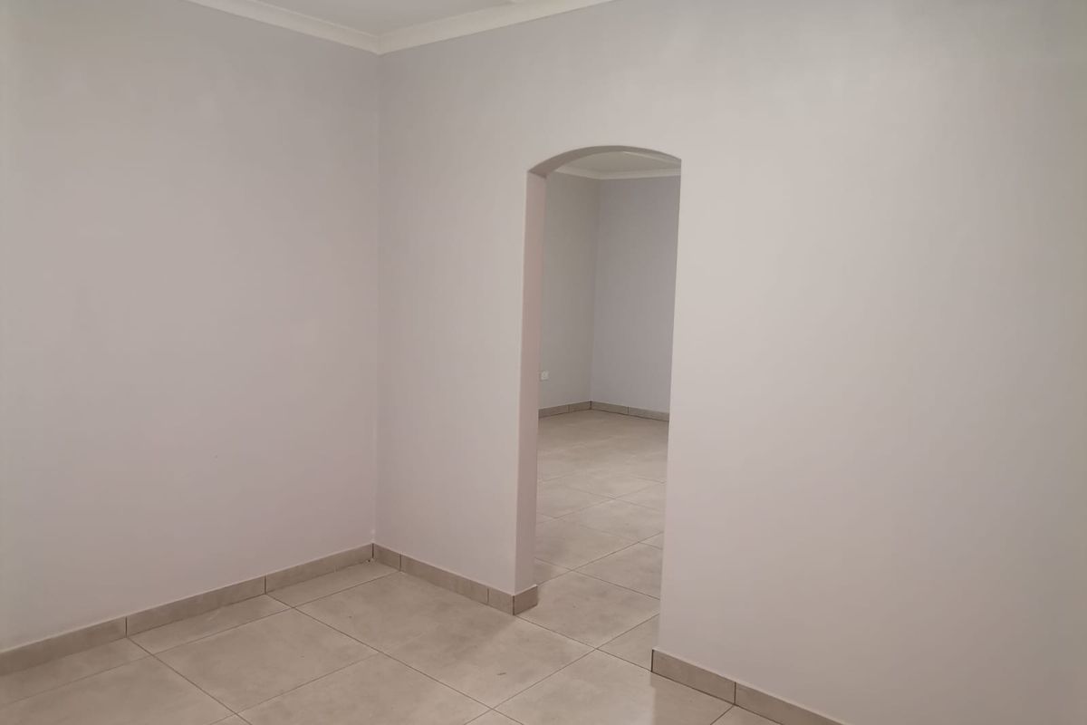 An empty interior space featuring neutral tiled flooring and a classic arched doorway leading into an adjoining room.