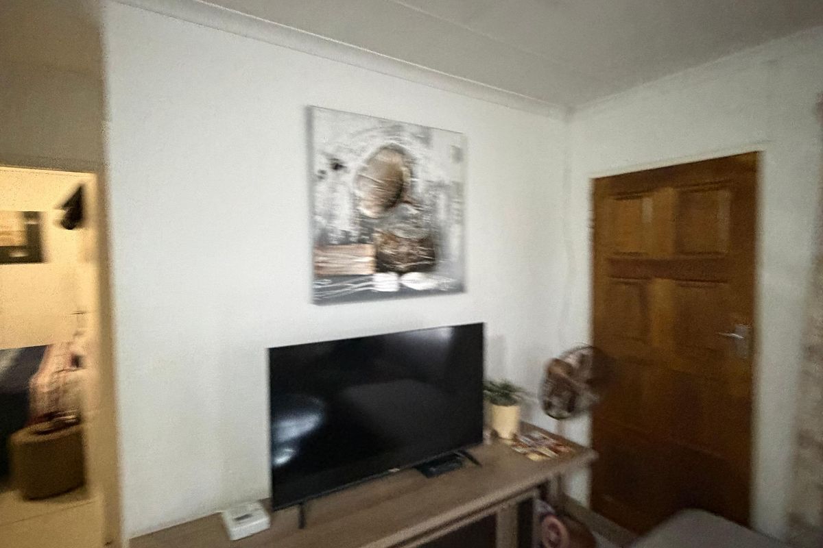 A living room area featuring tiled flooring, a wooden door, and a view into an adjacent room.