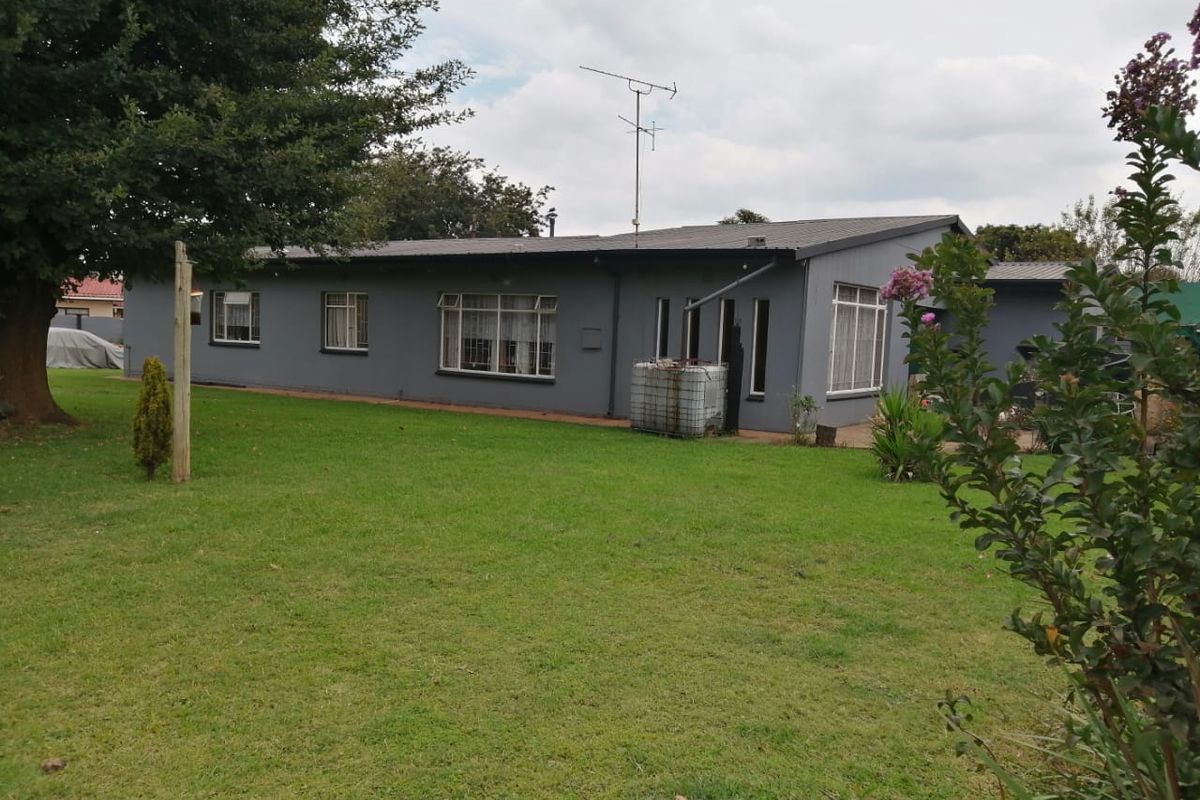Rear view of a single-story residential property featuring a large lawn, grey painted exterior walls, and tiled roofing.