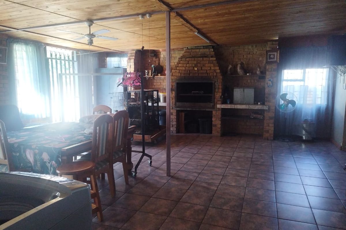 Spacious indoor entertainment area featuring a built-in brick fireplace, tiled flooring, and timber ceiling, suitable for casual gatherings and dining.