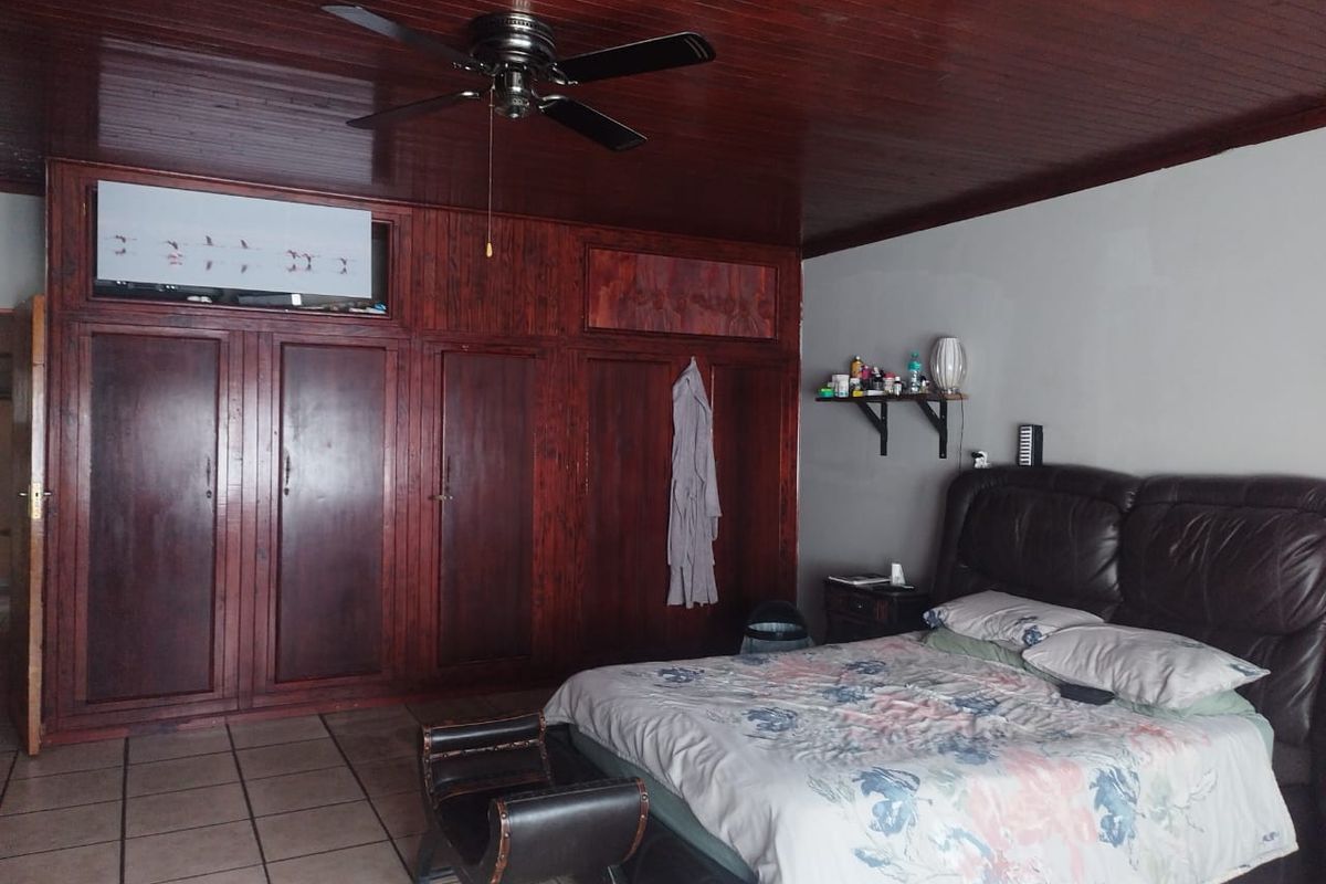 Spacious bedroom featuring extensive built-in wooden cabinetry, a dark wood-paneled ceiling with a ceiling fan, and tiled flooring.