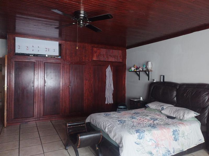 Spacious bedroom featuring extensive built-in wooden cabinetry, a dark wood-paneled ceiling with a ceiling fan, and tiled flooring.