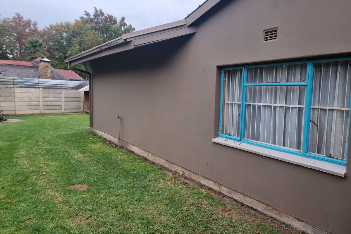Rear exterior view of the house featuring painted masonry walls, metal-framed windows with security bars, and a grassed backyard area.