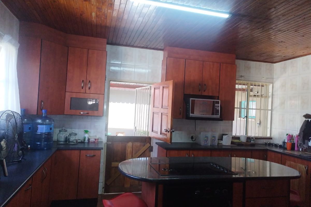 A functional kitchen featuring timber ceiling paneling, built-in cabinetry, dark countertops, and integrated cooking appliances with direct access to the exterior.