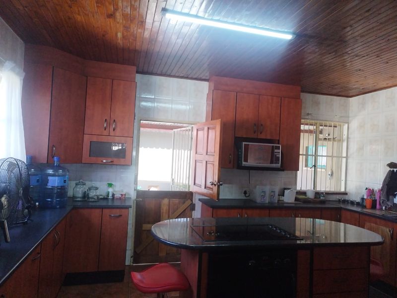 A functional kitchen featuring timber ceiling paneling, built-in cabinetry, dark countertops, and integrated cooking appliances with direct access to the exterior.