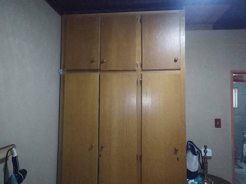 A bedroom featuring a full-height wooden built-in wardrobe with overhead storage compartments.