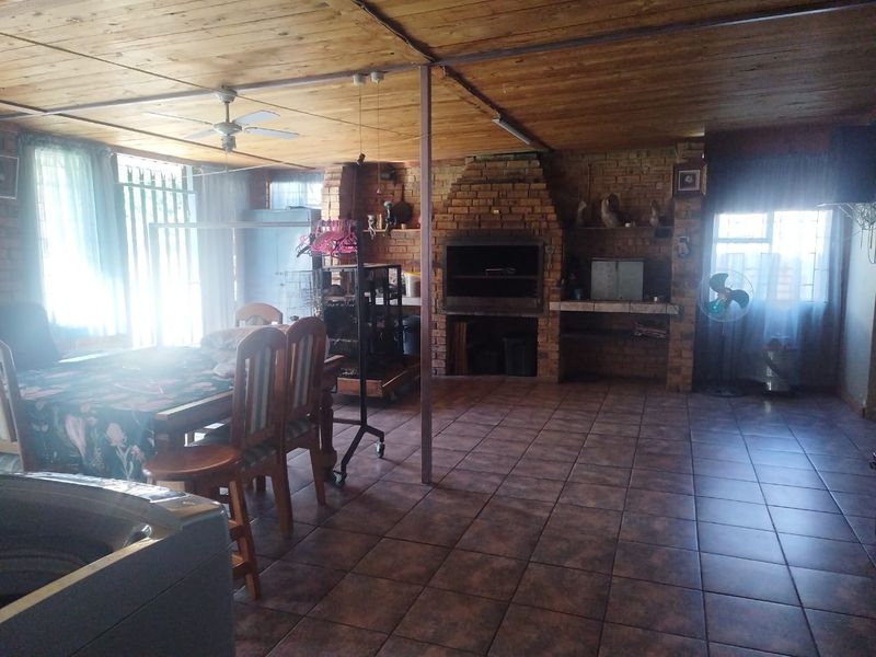 Spacious covered patio area featuring a built-in brick braai, exposed timber ceiling, and tiled flooring, ideal for outdoor entertaining.