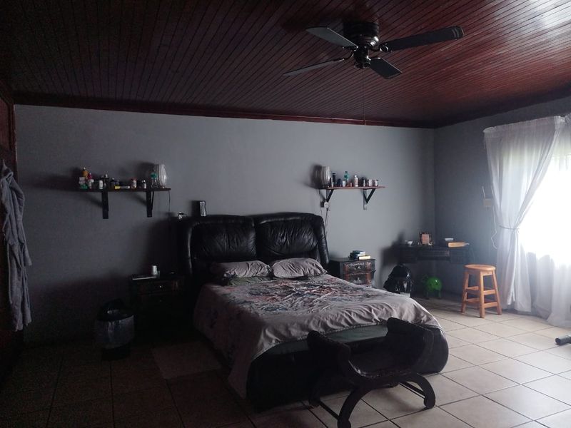 A bedroom featuring a dark timber ceiling, ceiling fan, and tiled flooring, providing a functional space with neutral wall tones.