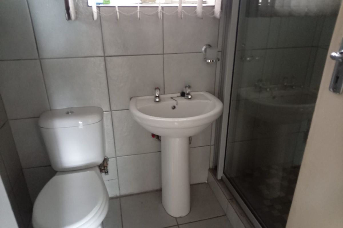 A functional bathroom featuring a pedestal sink, a standard toilet, and a glass-enclosed shower stall with tiled walls and flooring.